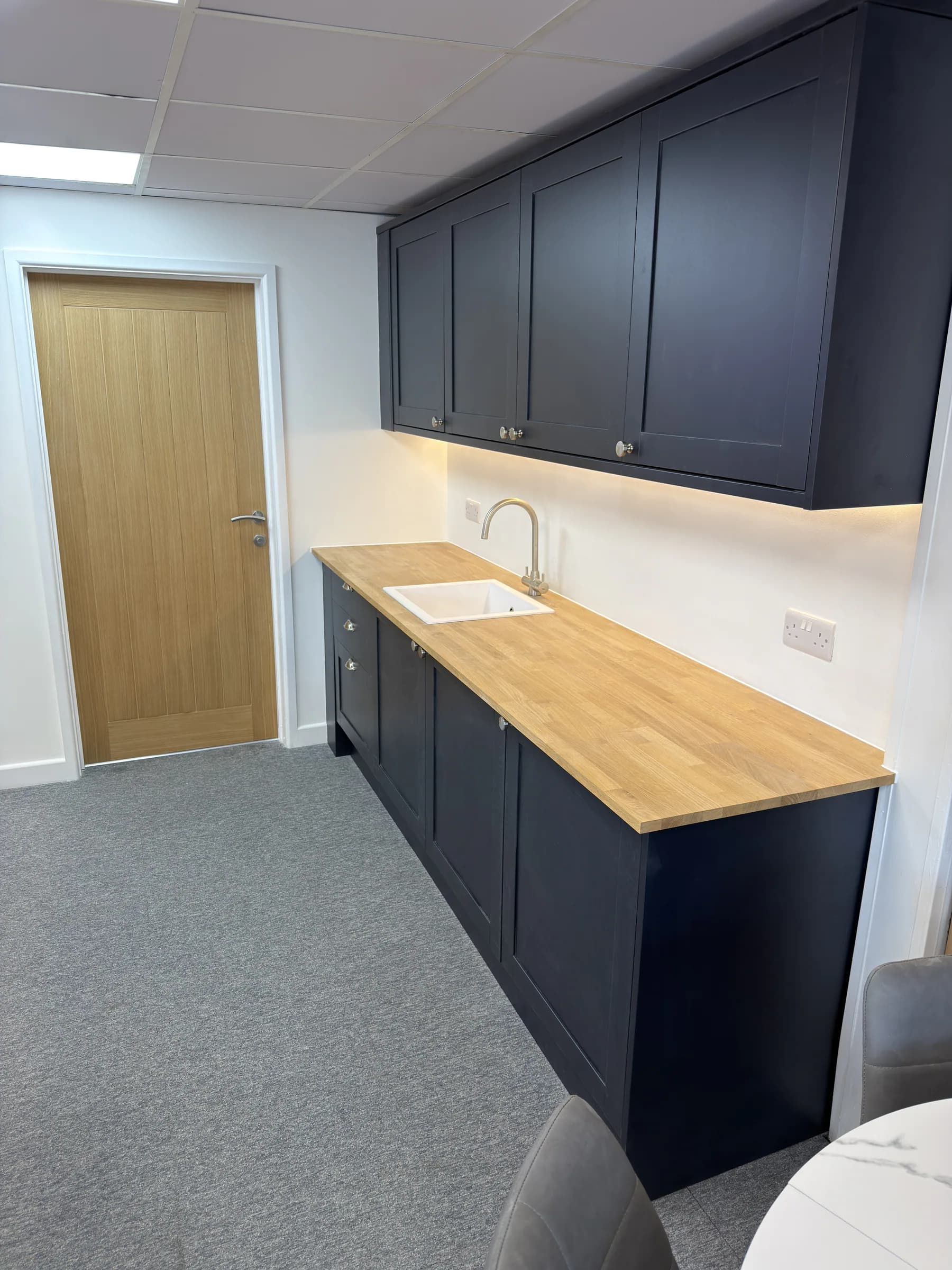 Dark fitted office kitchenette with an oak worktop and inset sink