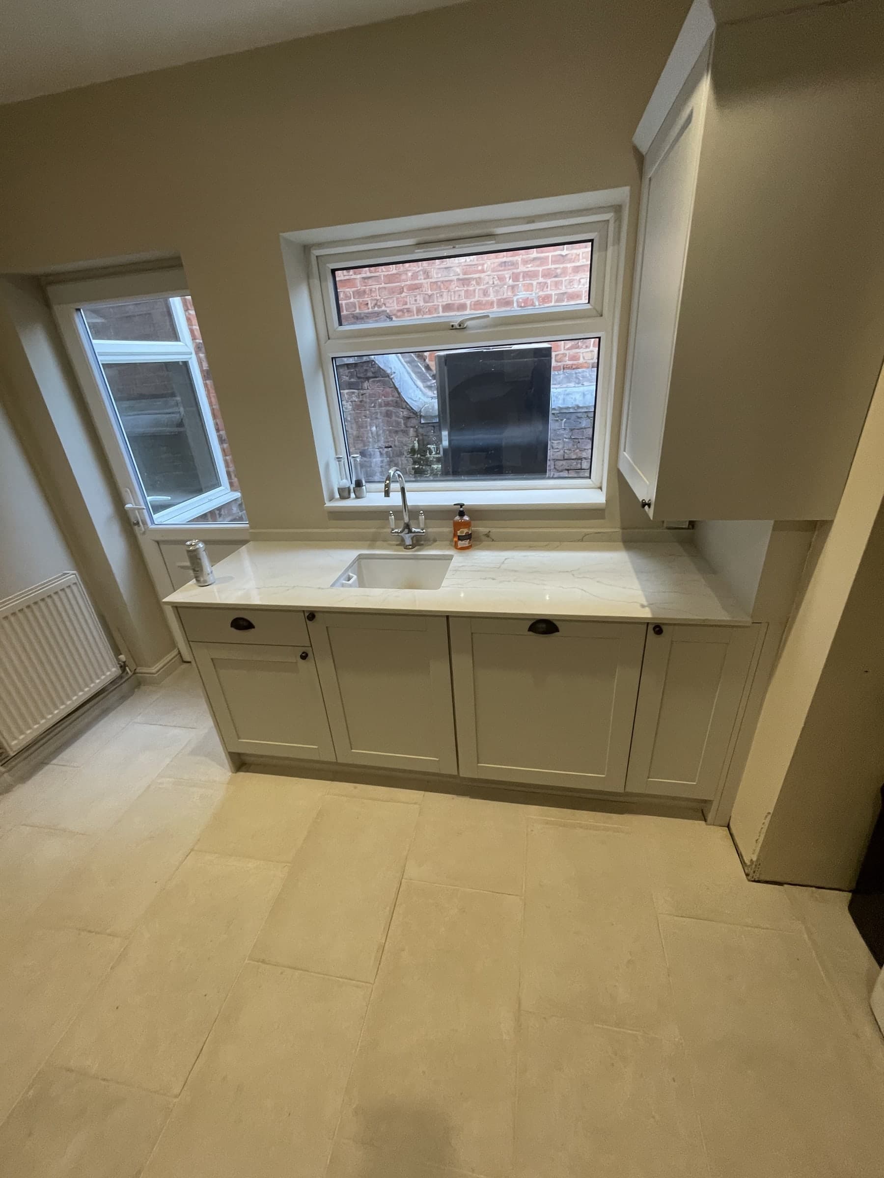 Completed kitchen sink area with fitted cabinet and window reveal
